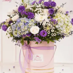 A full view of the purple and white floral arrangement, showing the volume and expert composition of the blooms within the pink box. Each flower is carefully placed to create a harmonious and luxurious feel.