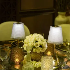 A complete tabletop centerpiece featuring a bouquet of white roses, elegant mini-lamps, and crystal candle holders on a mirrored base. This setup is the epitome of sophisticated dining.