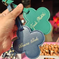A close-up of the elegant calligraphy on green and blue leather luggage tags. The gold ink adds a festive and luxurious feel, perfect for a wedding celebration.