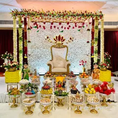 A beautiful all-white floral backdrop with red accents creates a very elegant and classic look. This setup for a baby shower combines a traditional frame with a modern color palette, complete with detailed plate arrangements and dolls.