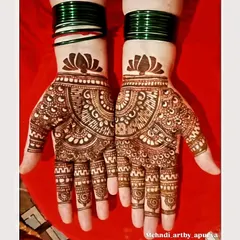 This is a classic palm-focused design with a lotus motif at the wrist and a detailed mandala pattern. The green bangles complement the henna beautifully, showing how it will look as part of a full outfit.