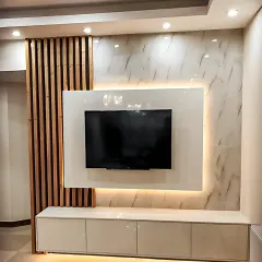This entertainment center features a floating white console and a glossy white TV panel set against a marble-effect wall. The design is accented with a vertical wooden slat element, combining minimalism with a touch of natural texture.