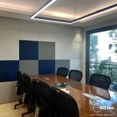 A clean and modern conference room with a large wooden table and ergonomic chairs. The wall features acoustic paneling in a checkerboard pattern to improve sound quality during important meetings.