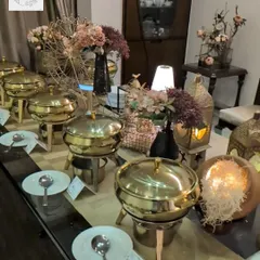 A beautiful buffet setup for a home party. We use golden chafing dishes, floral decor, and ambient lighting to create a warm and luxurious atmosphere for your guests.