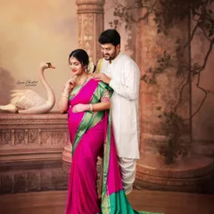 An elegant maternity portrait featuring a beautiful pink and green silk saree. The backdrop, reminiscent of ancient architecture, adds to the classic, painterly feel of the photograph.