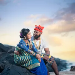 A romantic moment captured on the rocks by the sea. The couple, dressed in beautiful Agri-Koli attire, shares a look as the sun sets, creating a warm and intimate pre-wedding photograph.
