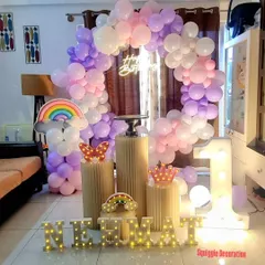 A lovely rainbow-themed first birthday party for a home celebration. The decoration features a pastel rainbow balloon arch, a light-up 'ONE', and cute rainbow and butterfly props.