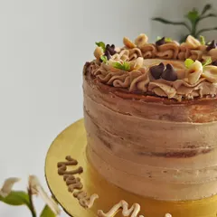 A side view of the vanilla and Biscoff cake, showing the rustic textured frosting and the personalized message written on the cake board.