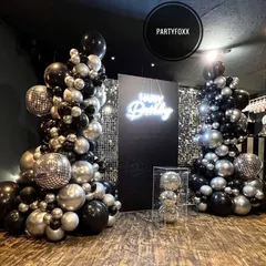 A chic and modern birthday setup with black and silver balloon towers, disco balls, and a neon "Happy Birthday" sign against a sequin backdrop.