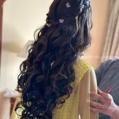 A whimsical half-updo with soft curls, adorned with delicate butterfly clips and a sparkling gold accessory. This is a perfect hairstyle for a dreamy and romantic Mehendi look.
