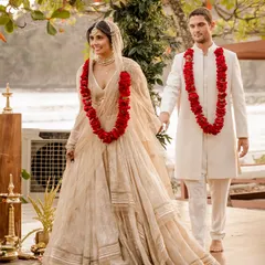 The couple walking hand-in-hand after their ceremony. Her Tarun Tahiliani lehenga and his Lalit Laungani sherwani, both in ivory, created a perfectly coordinated look against the lush greenery.