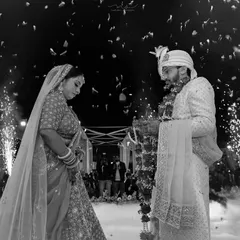 We capture the dramatic and emotional peak moments of your wedding day. This black and white photograph shows the bride and groom during the Varmala ceremony, framed by fireworks and smoke for a truly cinematic feel.