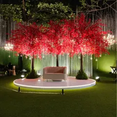A striking reception stage featuring two large, crimson cherry blossom trees. The minimalist pink sofa sits on a circular white stage, creating a dramatic and modern centerpiece for the celebration.