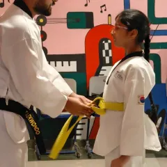 A proud moment for every student: earning their next belt. We focus on personal attention and guidance, helping each student, like this young girl receiving her yellow belt, progress with confidence.
