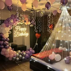 This birthday room decoration combines a beautiful balloon arch with a neon sign and a cozy canopy over the bed. The purple, pink, and silver color scheme creates a dreamy and elegant atmosphere for a special celebration.