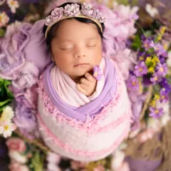 A detailed close-up of the baby in a textured, multi-toned wrap with a matching lavender floral crown. This angle emphasizes the serene expression and delicate features of the newborn.