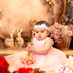 A lovely portrait from a 6-month-old's sitter session. Dressed in a soft pink tulle dress, she is sitting in a whimsical studio setting decorated with flowers and adorable bunny figurines, creating a gentle, storybook feel.