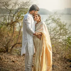 An expecting couple, dressed in beautiful traditional Indian attire, shares a tender moment by a lakeside. The husband gently kisses his wife's forehead, creating a serene and romantic maternity portrait.