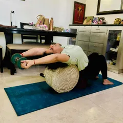 To open the shoulders for deeper backbends, we use props. Here, a student uses a bolster for support and light dumbbells to add gentle weight, increasing the stretch across the chest and front deltoids.