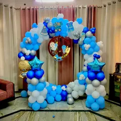Another view of a home-based celebration for a baby boy. The balloon ring is decorated with cute baby-themed cutouts and foil balloons, transforming the living room into a party zone.