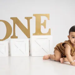 Marking the journey to one year old with a pre-birthday milestone shoot. This photo captures a baby on the move, crawling past large "ONE" props in a clean, minimalist setting.