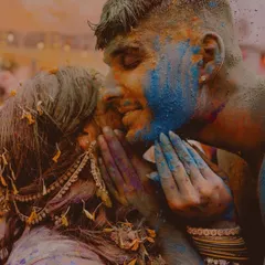 A powerful, close-up moment of a kiss during a vibrant color or Haldi celebration. The image is filled with raw emotion, color, and texture, capturing a moment of pure, passionate joy that is completely unscripted.