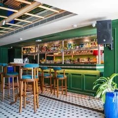 The bar area, complete with tall, solid wood bar stools with comfortable turquoise upholstered seats. These were designed to be both sturdy for a busy bar and stylish to match the overall green and white aesthetic.