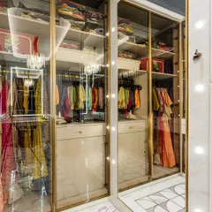 A close-up of the glass-fronted cabinets, which beautifully display a collection of traditional Indian wear. The integrated lighting ensures every item is perfectly illuminated.