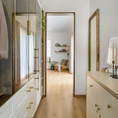 This walk-in closet in 'House of Kismish' features a beautiful combination of white PU-finished drawers, brass hardware, and wood-and-glass shutters.