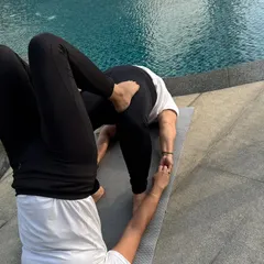 A creative partner pose by the pool, demonstrating trust and core control. One yogi holds a stable headstand while the other balances in a bridge pose variation on top.