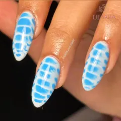 A stunning design in white and blue. This close-up shows the intricate, almost water-like pattern on these long almond nails.