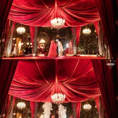 The Varmala ceremony framed by dramatic red drapery and elegant chandeliers. This shot highlights the grandeur of the decor while keeping the focus on the couple's intimate moment of exchange.