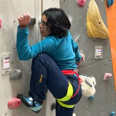 A first time climber focuses on her footwork and grip as she makes her way up a beginner route. Notice her chalk bag, an essential piece of gear we provide to help with grip.