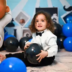 Another little one enjoying our Boss Baby setup. The decor uses a consistent color scheme of blue, black, and white, with plenty of balloons for the child to interact with.