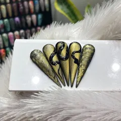 This set of five stiletto nail tips displays an impressive hand-painted black snake design over a textured gold and black gradient background. It's a powerful and luxurious example of our custom, high-fashion nail art.