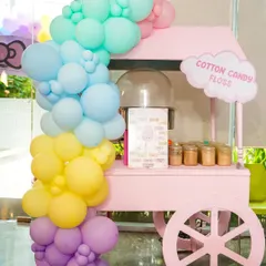 A pink cotton candy cart with a pastel balloon arch, ready to spin sweet treats for guests.