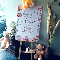 The welcome setup for the rustic baby shower, featuring a personalized sign on an easel, flanked by cute teddy bears and a vase of pampas grass to introduce the theme.