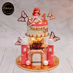 This two-tier chocolate castle cake is fit for a princess's first birthday. It features a detailed fondant castle design, a light-up spacer for a magical glow, and a charming princess toy topper.