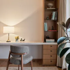The study nook within the NG Penthouse continues the theme of clean lines and warm materials. A floating stone desk is paired with built-in wooden shelving, creating a functional workspace that feels integrated and uncluttered.