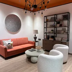 Another view of my studio's lounge area, designed for informal meetings and brainstorming. The combination of the warm orange sofa, textured white chairs, and industrial-style shelving creates a balanced and eclectic workspace.
