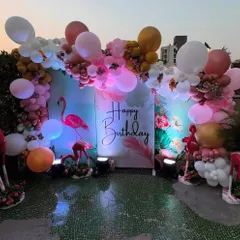 A beautiful flamingo-themed birthday on a rooftop, with a tropical print backdrop, flamingo props, and a pink and white balloon arch.