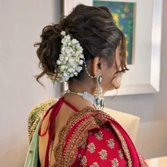 A detailed view of a traditional bridal updo, intricately woven and adorned with fresh jasmine flowers, or gajra. This classic hairstyle is perfect for wedding ceremonies, offering a timeless elegance that complements traditional Indian bridal wear.