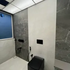 Another view of the Sanpada bathroom, highlighting the combination of dark and light grey tiles. The wall-mounted toilet and concealed cistern help create a clean, uncluttered floor space.