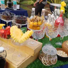 A beautiful display of fresh fruit garnishes. Sliced oranges, strawberries, pineapple, and whole berries are presented in elegant glassware, ready to be added to refreshing summer cocktails for a wedding brunch.