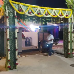 A traditional wedding entrance made from woven green coconut leaves. The structure is decorated with garlands of jasmine and red roses, creating an authentic and auspicious welcome for guests.