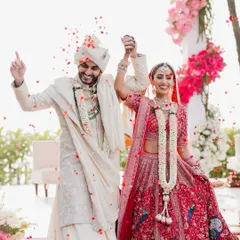 A celebratory moment as the newly married couple walks down the aisle, hands raised in triumph while being showered with flower petals.