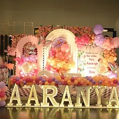 A full stage view for Aaranya's butterfly party, showcasing the large marquee letters, a multi-layered backdrop with a floral ring, and whimsical mushroom props.