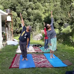 Leading a small group in an upward salute pose (Urdhva Hastasana) in the green fields of Dharmkot. The fresh mountain air makes the practice even more special.