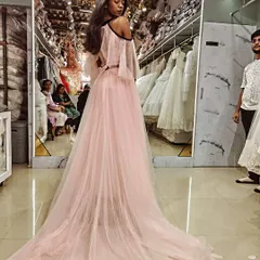 A beautiful client trying on her custom pink gown with a dramatic train. The cold-shoulder design and floral appliqués were details we chose together to create her dream look.