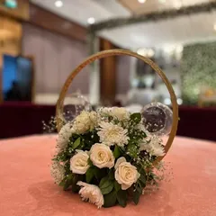 A close-up of a delicate and modern table centerpiece. This arrangement at Crowne Plaza Okhla features white roses and baby's breath inside a golden ring structure with hanging glass votives.
